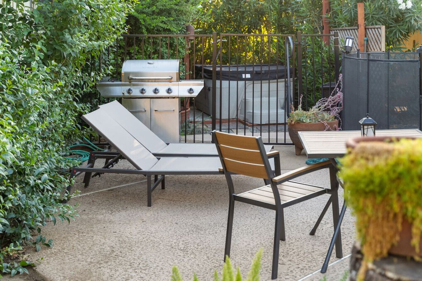 An outdoor patio with a grill, lounge chairs, and a table.