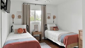 Un dormitorio con dos camas, ventilador de techo, ventana con cortinas, mesitas de noche y lámparas de pared.