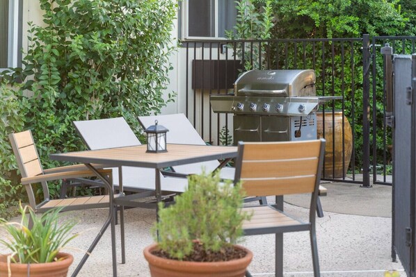 Un patio exterior con una mesa, sillas, una parrilla y plantas en macetas.