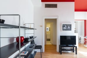 A modern living room with a TV, shelves, and a dining area.