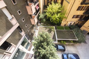 Vue aérienne d’un immeuble résidentiel à plusieurs étages, doté de balcons, avec un arbre et une voiture garée.
