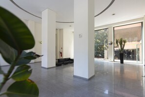 Un hall d’hôtel moderne au design épuré et minimaliste, avec une grande entrée vitrée, un extincteur et une plante en pot.