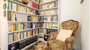 A library with bookshelves filled with books, a chair with a cushion, and a tiled floor. - Gordigiani Apartment (Firenze)
