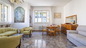 A spacious living room with a dining area, a large window with a view, a chandelier, and a fireplace. - Gordigiani Apartment (Firenze)