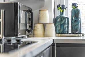 A kitchen counter with stacked cups labeled 'tea' and 'coffee', two vases with flowers, and a coffee machine. - Superb 3bed Fulham Palace Retreat (London)