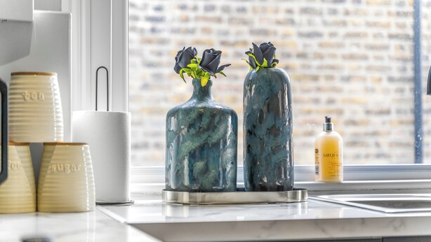 Una encimera de cocina con dos jarrones decorativos con flores, una taza blanca y una botella de jabón Baylis.