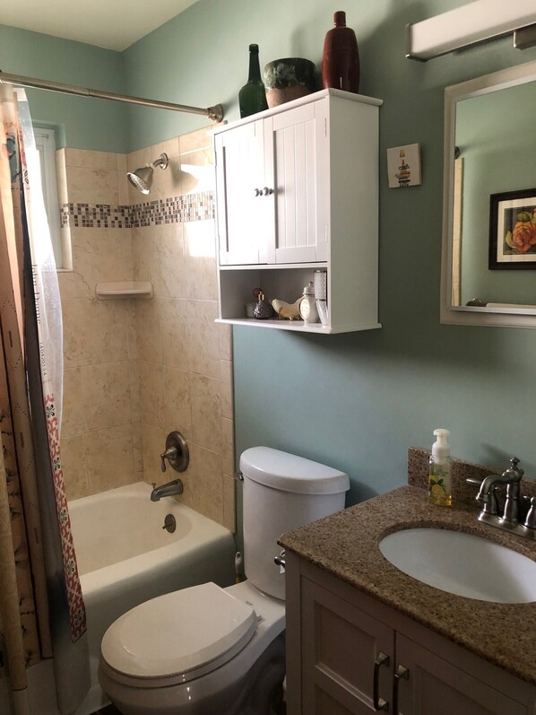 A bathroom with a bathtub, toilet, and sink. There are cabinets above the sink and a shower curtain.