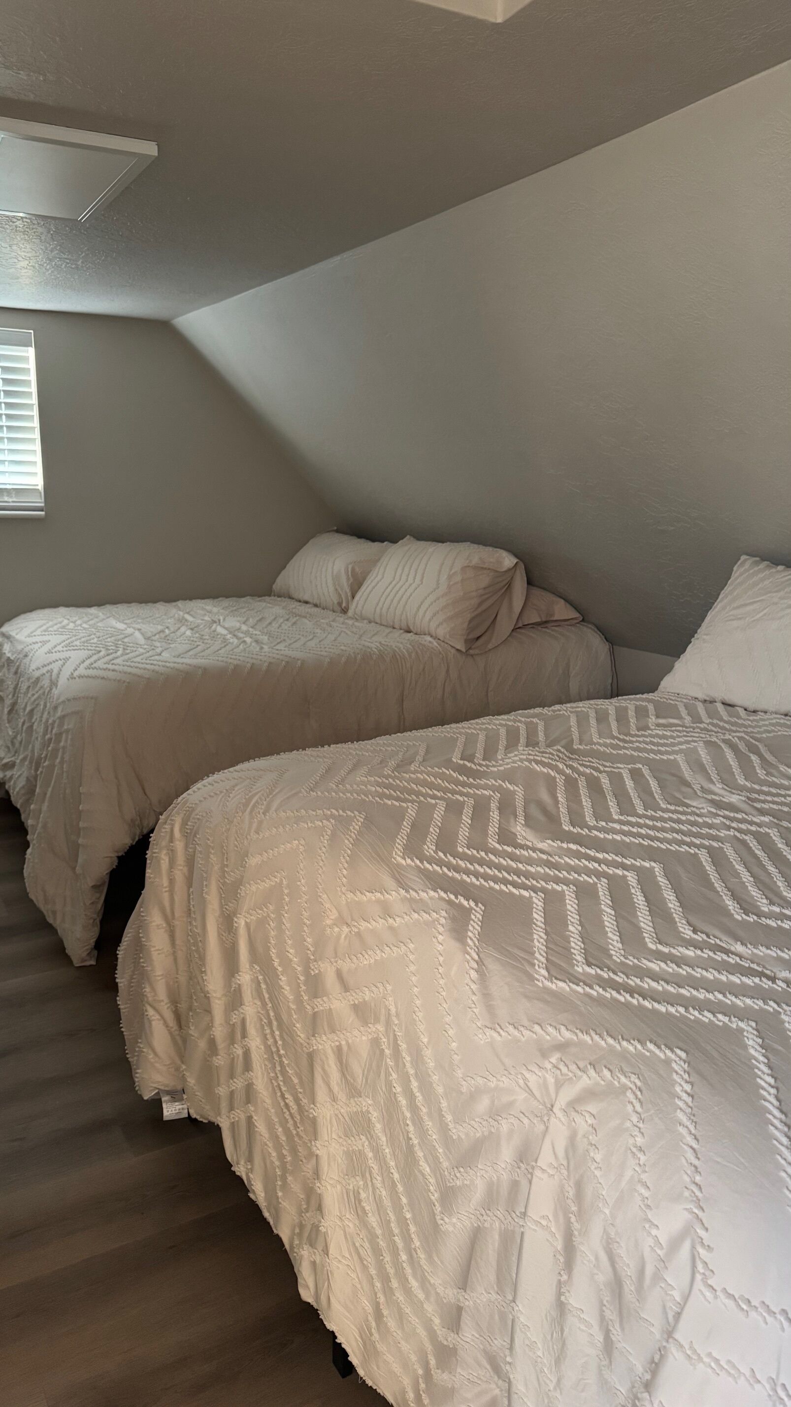 Camera da letto con due letti, un soffitto spiovente e una finestra con persiane.