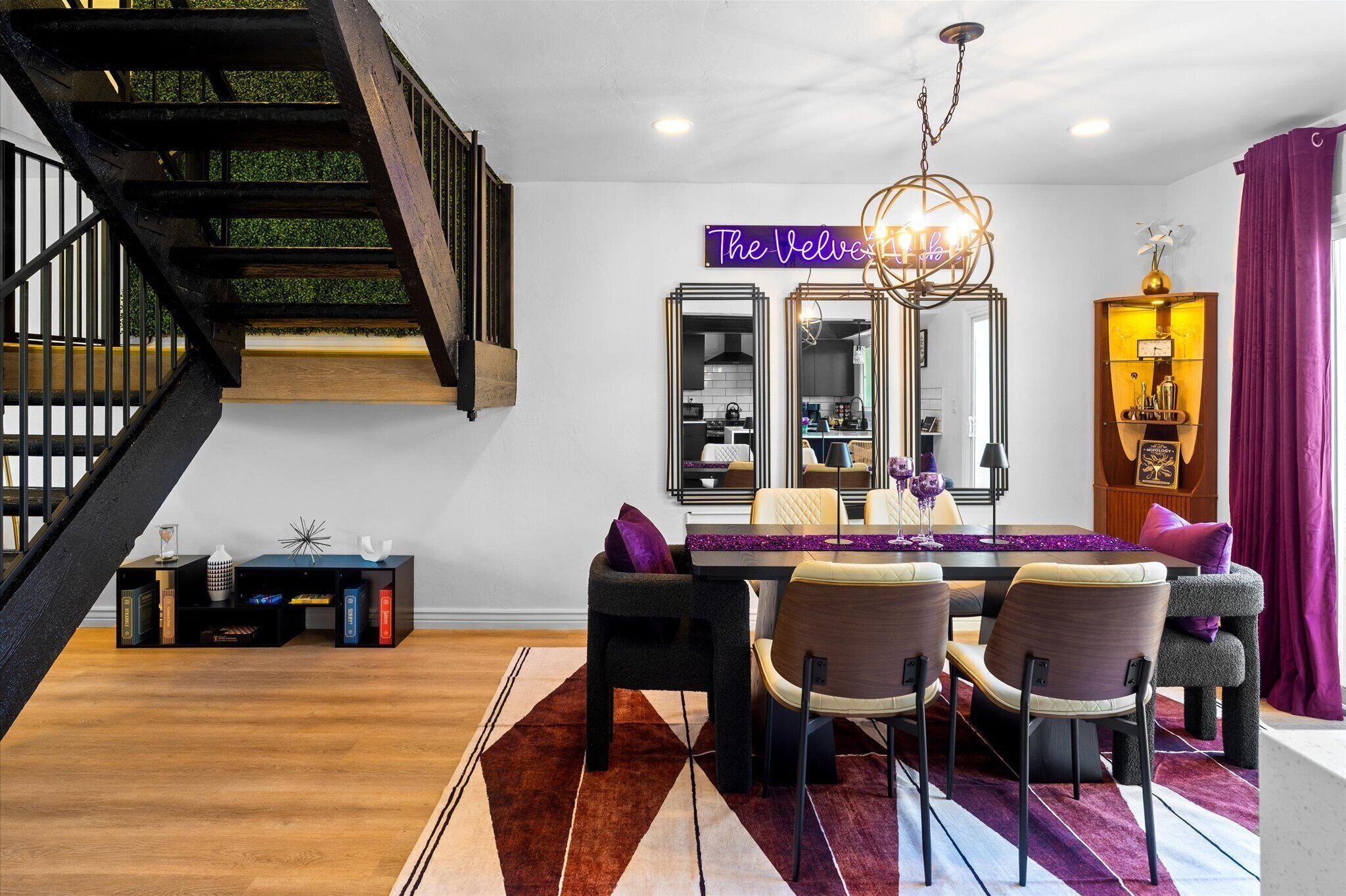 A dining area with a wooden staircase, a neon sign, and a chandelier.
