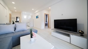 Ein modernes Wohnzimmer mit einem grauen Sofa, einem Flachbildfernseher und einem weißen Couchtisch mit einer Pflanze.