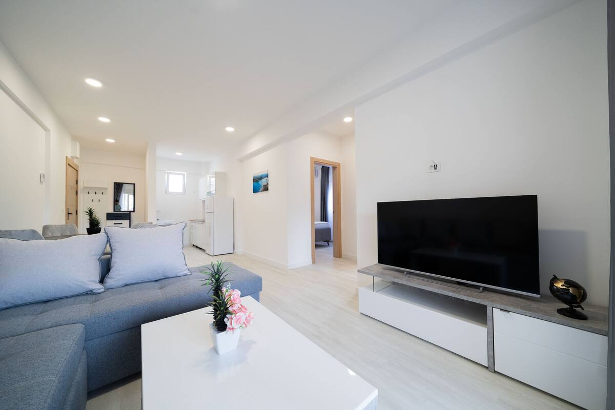 A modern living room with a grey sofa, a flat-screen TV, and a white coffee table with a plant.