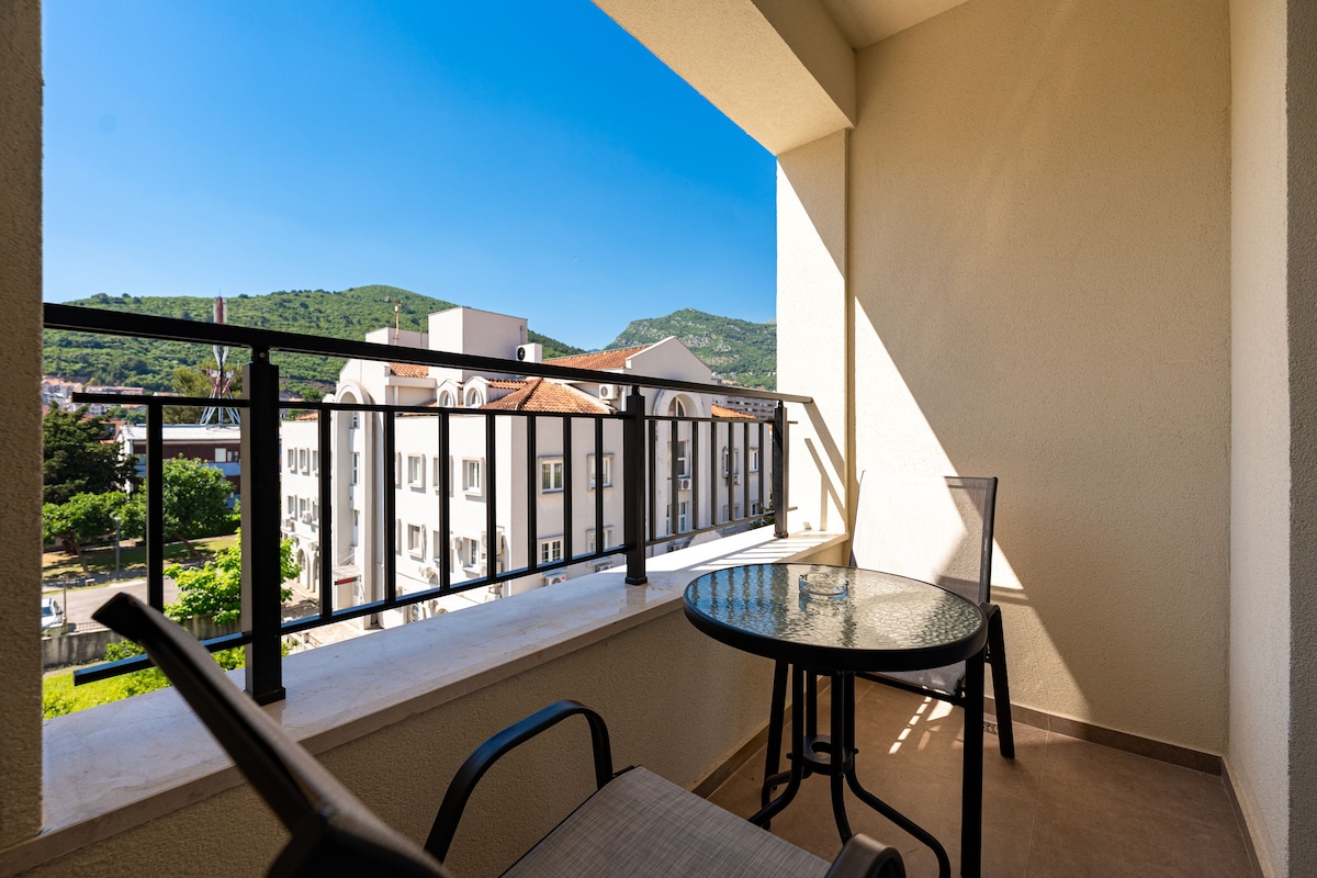 Ein Balkon mit Tisch und Stühlen, der einen Blick auf Gebäude und Grünflächen bietet.