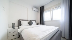 Ein modernes Schlafzimmer mit einem großen Bett, einem Nachttisch mit Lampe und einem Fenster mit Vorhängen.