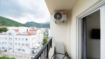 A balcony with a view of buildings and mountains, a fan, and a chair.