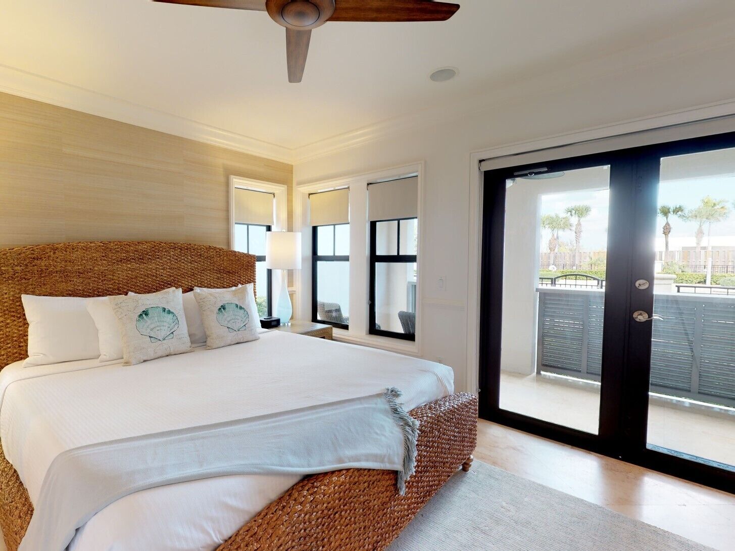 A bedroom with a large bed, a ceiling fan, and a view of the outdoors through a sliding glass door.