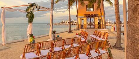 A beachside wedding setup with wicker chairs and a white canopy.