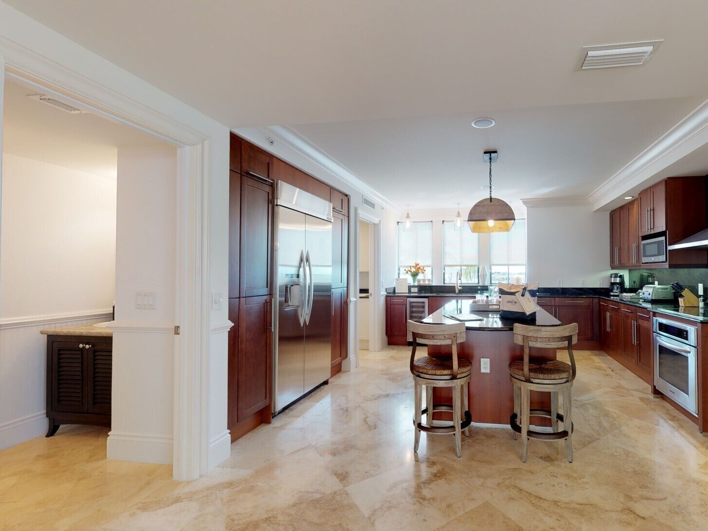 Una cocina moderna con una isla central, armarios de madera oscura, electrodomésticos de acero inoxidable y piso de mármol.