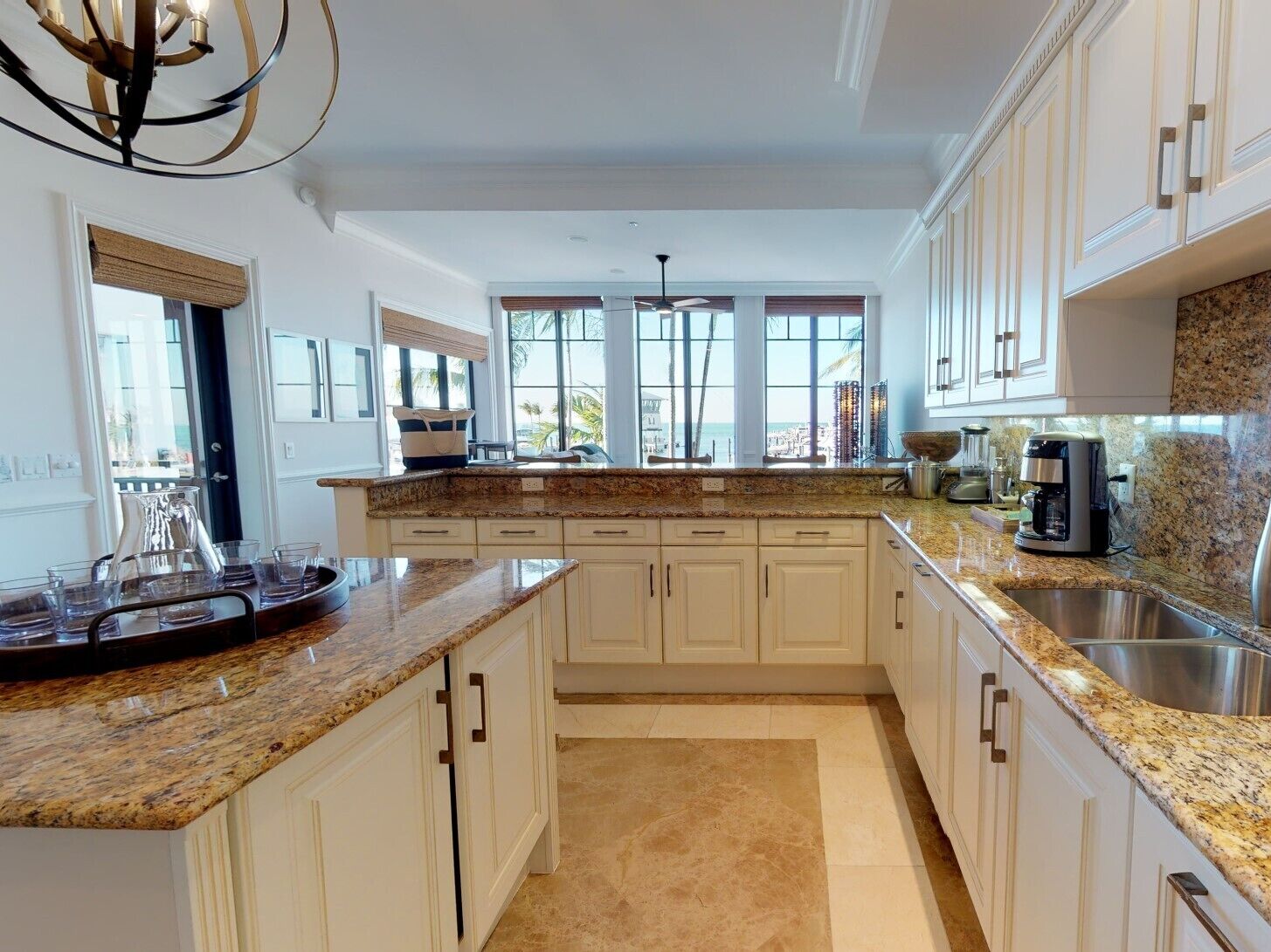 A spacious kitchen with white cabinetry, granite countertops, and a large window offering a view of the beach.