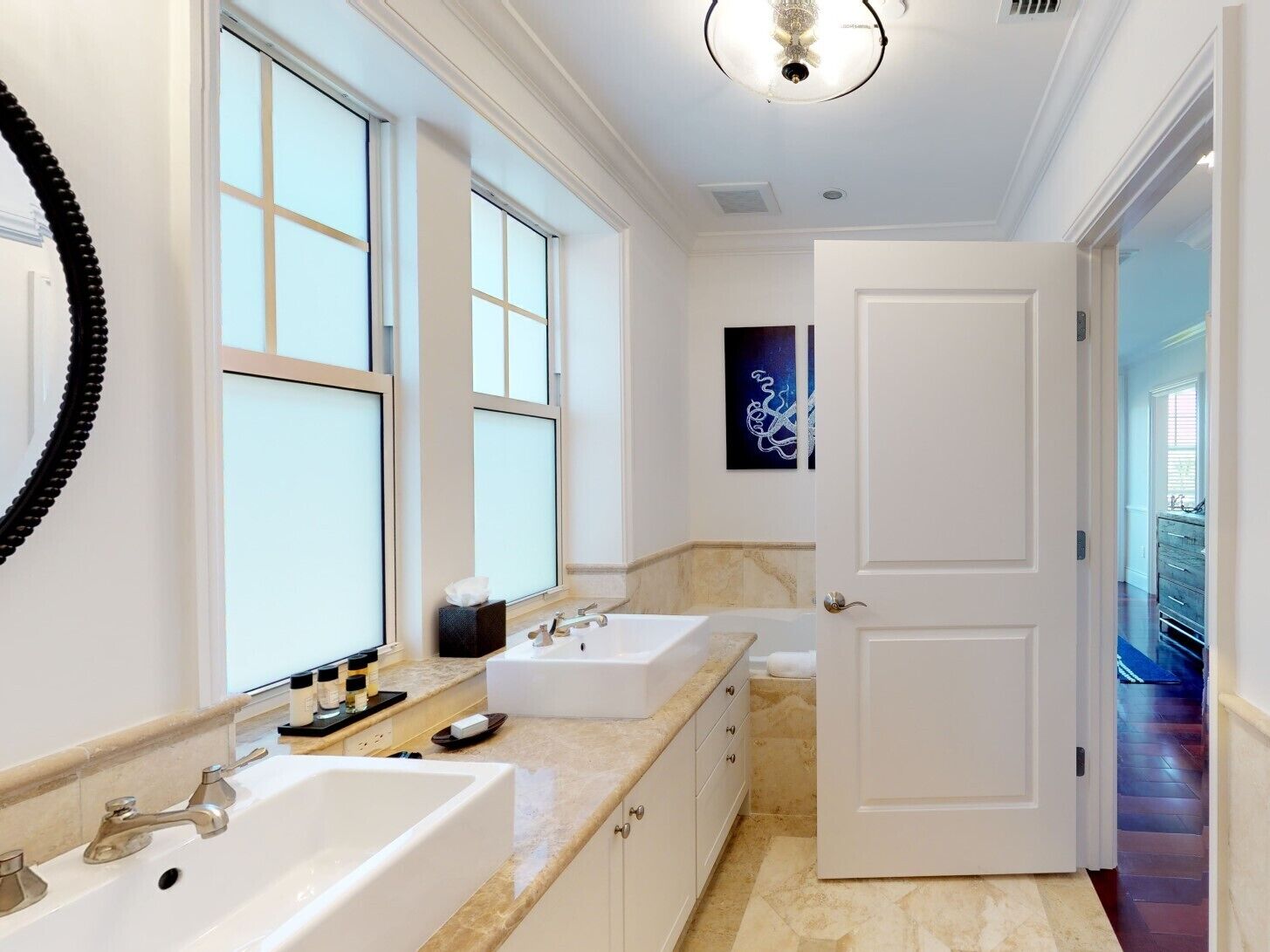 A modern bathroom with two sinks, a large mirror, and a door leading to a hallway.