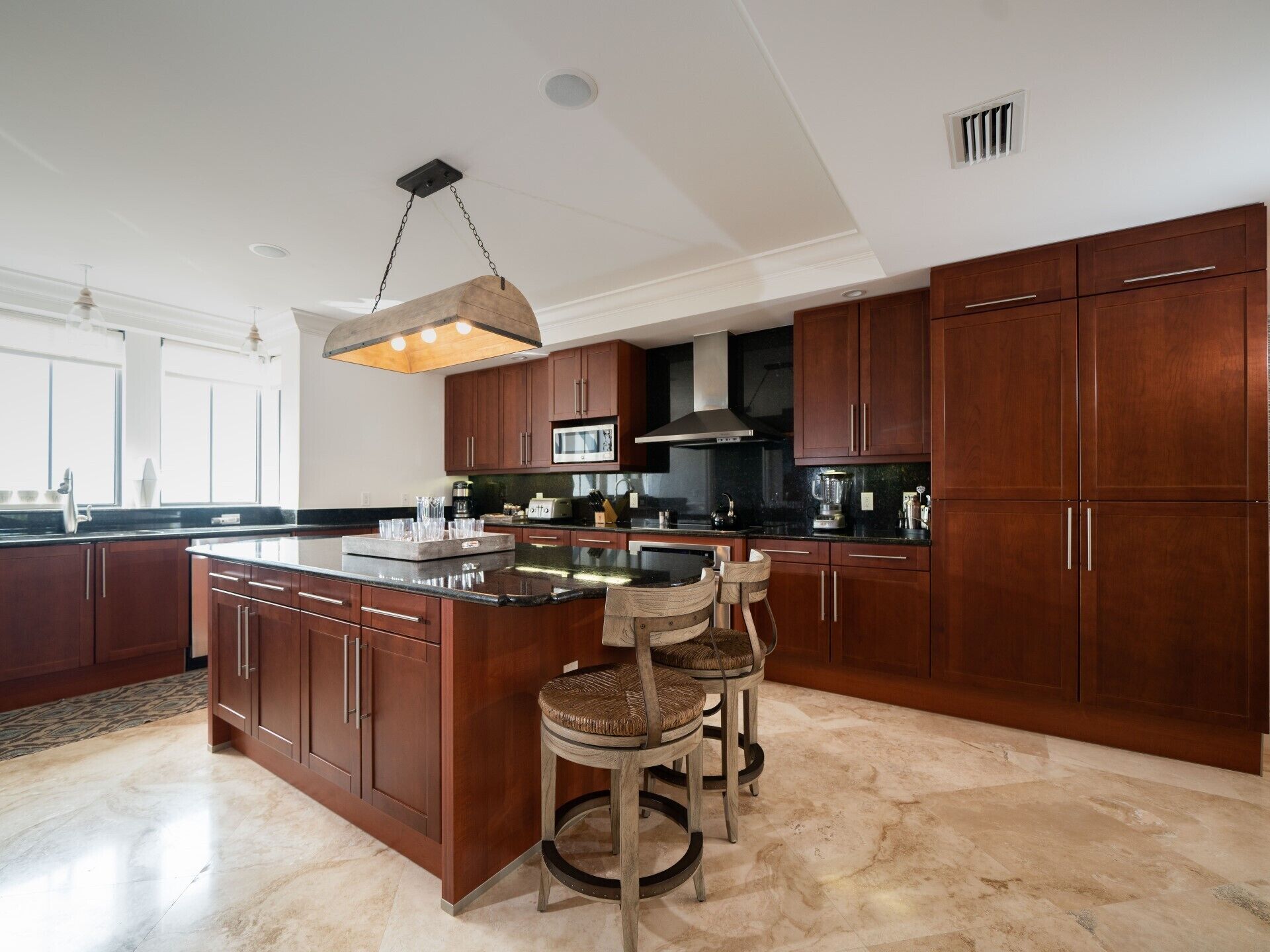 A modern kitchen with dark wood cabinets, a large island with bar stools, a hanging light fixture, and a microwave above the island.
