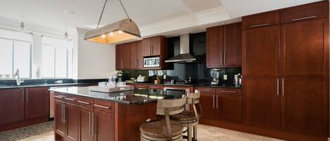 A modern kitchen with dark wood cabinets, a large island with bar stools, a hanging light fixture, and a microwave above the island.