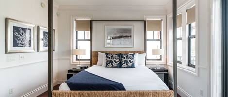 A hotel room with a large bed, two bedside tables, a wall-mounted artwork, and a view of the outdoors through the window.