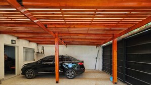 A garage with a black car parked inside, wooden beams on the ceiling, and a concrete floor.