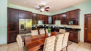 A modern kitchen with dark wooden cabinets, a stainless steel refrigerator, a dining table with chairs, and a ceiling fan. - Las Brisas 1-1 • 3 BR Beach-Front Condo • Salt-Water Pool & Walk to Playa Hermosa • 6 Guests (Playa Hermosa)