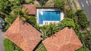 An aerial view of a resort with a central swimming pool, surrounded by lush greenery and two large, tiled-roofed structures. - Las Brisas 1-1 • 3 BR Beach-Front Condo • Salt-Water Pool & Walk to Playa Hermosa • 6 Guests (Playa Hermosa)