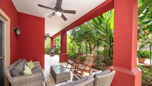 A covered outdoor seating area with wicker furniture, a ceiling fan, and a view of lush greenery. - Las Brisas 1-1 • 3 BR Beach-Front Condo • Salt-Water Pool & Walk to Playa Hermosa • 6 Guests (Playa Hermosa)