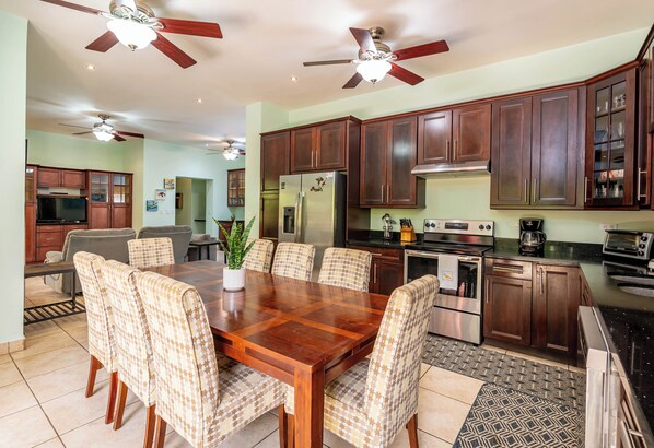 A spacious dining area with a wooden table and patterned chairs, surrounded by dark wooden cabinets and modern appliances. - Las Brisas 1-1 • 3 BR Beach-Front Condo • Salt-Water Pool & Walk to Playa Hermosa • 6 Guests (Playa Hermosa)