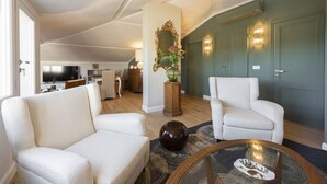 Een woonkamer met een bank, fauteuil en een salontafel. Er hangt een spiegel aan de muur en staat een vaas met bloemen.