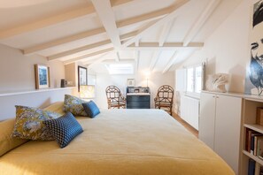 Um quarto com uma cama, duas cadeiras, uma cômoda e uma estante de livros.