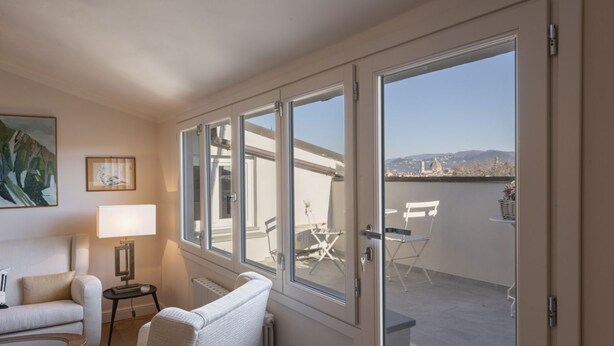 Een kamer met een bank, een stoel, een lamp en uitzicht op een balkon met buitenmeubilair.