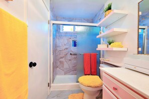 Un baño con ducha, inodoro y tocador con estantes.