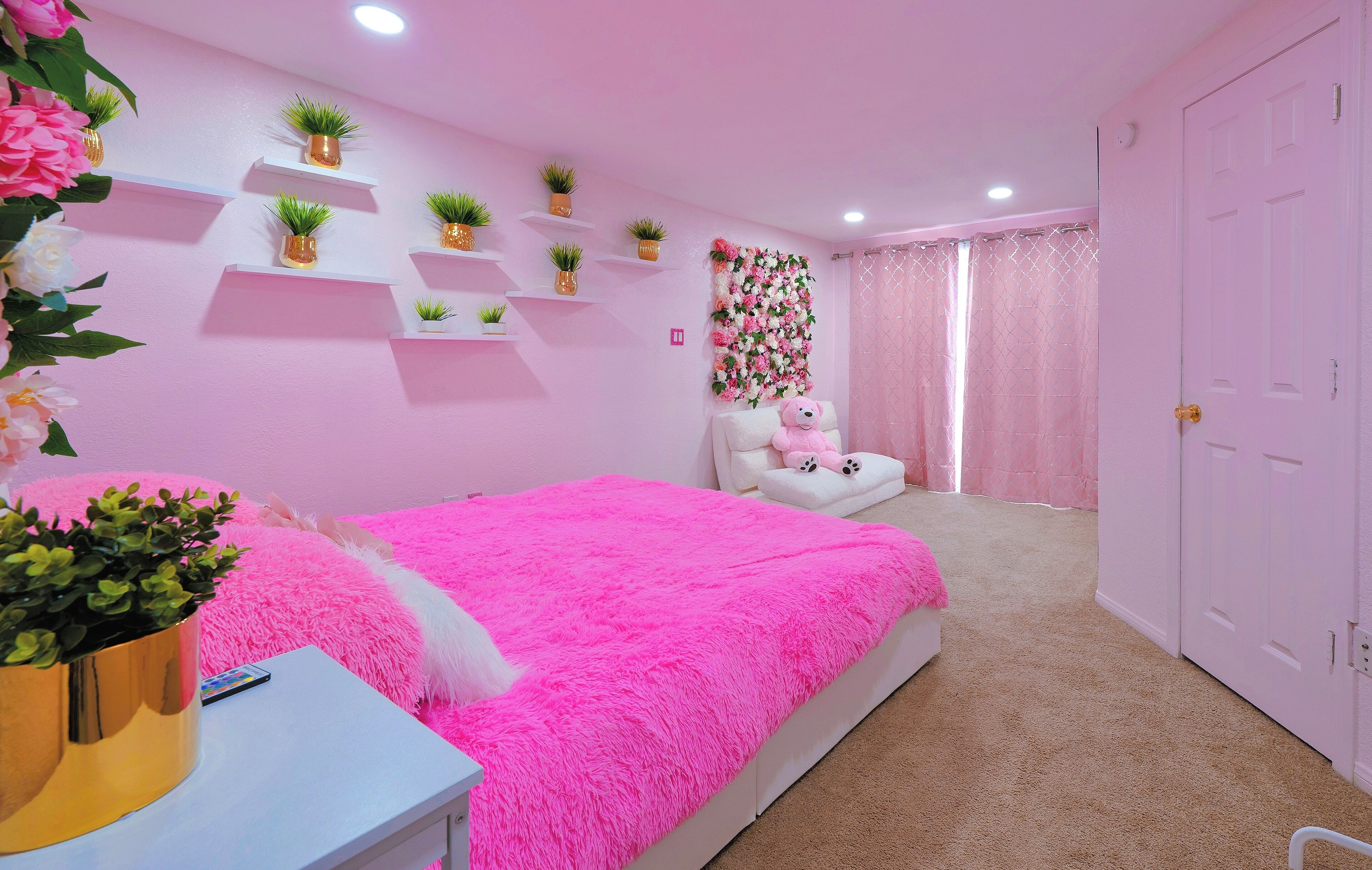 A pink-themed bedroom with a bed, a chair, and shelves with plants.