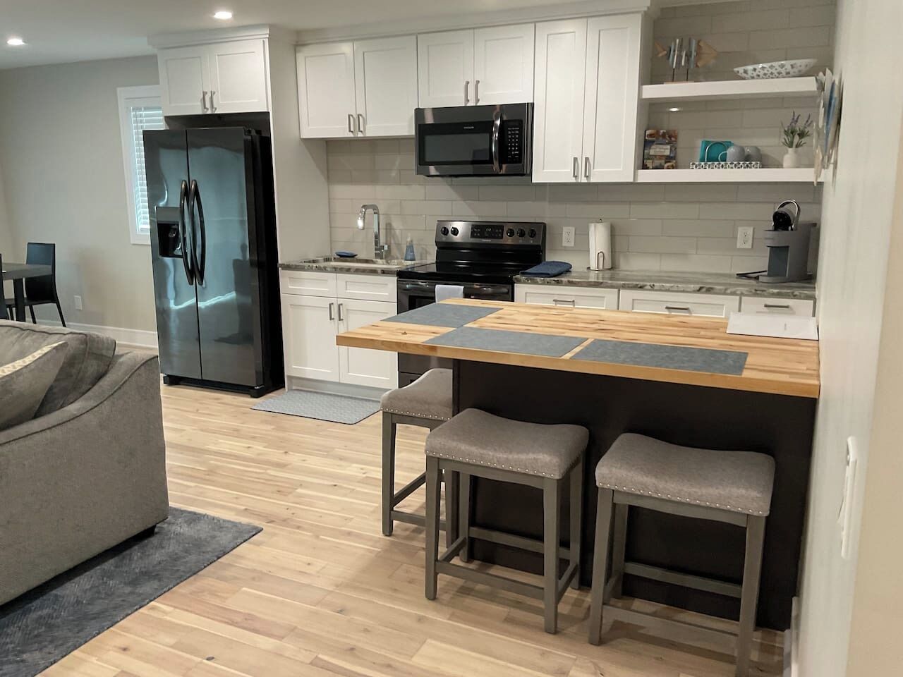 Una cocina moderna con refrigerador, microondas, estufa y taburetes de bar.