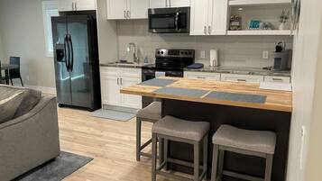 Una cocina moderna con refrigerador, microondas, estufa y taburetes de bar.