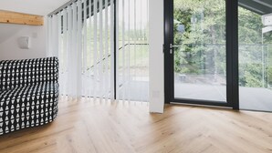 Ein modernes Zimmer mit einer gemusterten Couch, einer Treppe mit Glasgeländern und Blick auf Grünfläche vor dem Fenster.