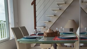 A dining area with a glass table, beige chairs, and a staircase in the background. - Villa 54 at Colibri d'Isa, a haven of peace between sea, mountains and rainforest (CAPESTERRE BELLE EAU)
