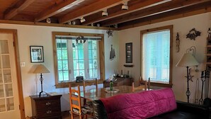 Un salon chaleureux avec un plancher en bois, un canapé en cuir noir, une chaise en bois, une petite table avec une lampe et une fenêtre équipée de stores.