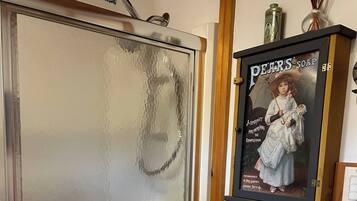 Un baño con cabina de ducha de vidrio, un inodoro blanco y un anuncio enmarcado de Jabón Pears.