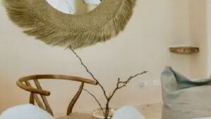Una sala de estar con un espejo redondo, una silla de madera y una planta pequeña.