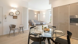 A modern kitchen with a built-in oven, a dining area with a glass table and chairs, and a living area with a sofa and a coffee table. - Central Station Apartment – Modern Comfort in the Heart of Bari (Bari)