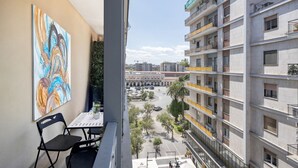 A balcony with a table and chairs, overlooking a cityscape with buildings and a plaza. - Central Station Apartment – Modern Comfort in the Heart of Bari (Bari)