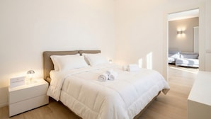A modern bedroom with a bed, nightstand, and a view of another room. - Central Station Apartment – Modern Comfort in the Heart of Bari (Bari)