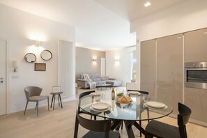 Une cuisine moderne dotée d’un four encastré, un coin repas avec une table et des chaises en verre, et un salon avec un canapé et une table basse.