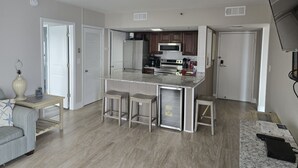 A modern kitchen with a central island, stainless steel appliances, and a dining area with a light-colored sofa and a small table. - Sunset Palace Perfect Beach Getaway: Stunning Updates & Unbeatable Convenience! (Myrtle Beach)