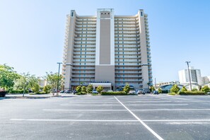 Un hôtel à plusieurs étages, doté d’un élément vertical central, d’un parking et d’un espace vert environnant.
