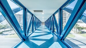 Un couloir doté de fenêtres en verre teinté de bleu et d’un sol à motifs, qui mène à l’entrée d’un bâtiment.